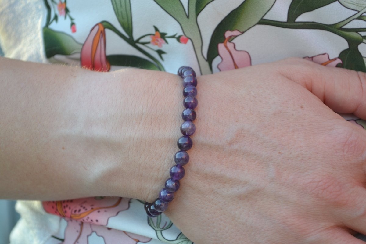 Bracelet Améthyste en pierre naturelle porté sur un poignet d'une femme au niveau du ventre. perle de diamètre 5-6mm