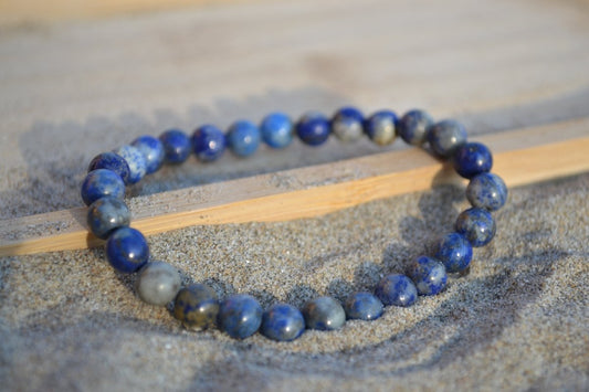 Bracelet Lapis Lazuli en pierre naturelle posé sur du sable à cheval sur un plateau en bois. perle de diamètre 5-6mm