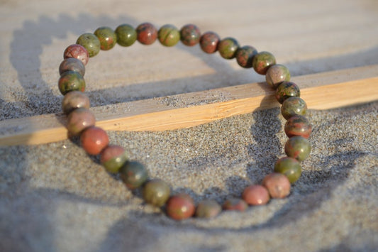 Bracelet Unakite en pierre naturelle posé sur du sable à cheval sur un plateau en bois. perle de diamètre 5-6mm