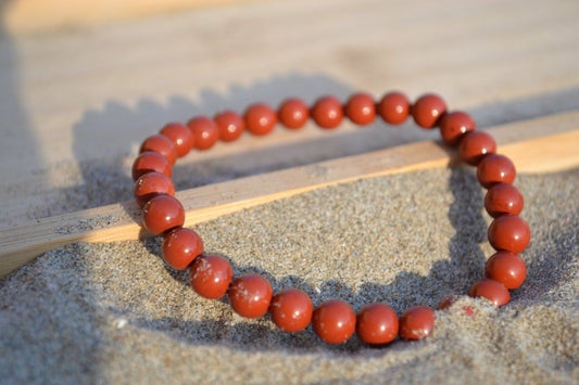 Bracelet Jaspe Rouge en pierre naturelle posé sur du sable à cheval sur un plateau en bois. perle de diamètre 5-6mm