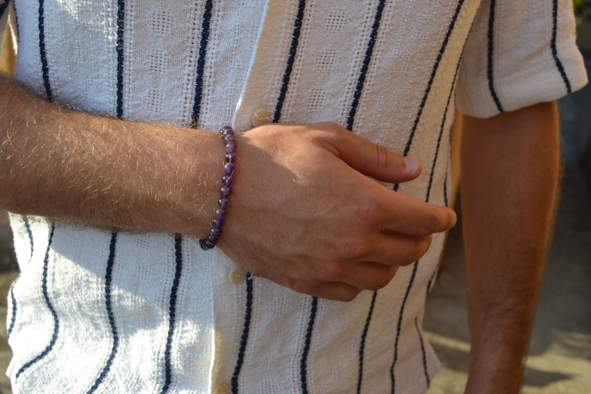 Bracelet Améthyste en pierre naturelle porté sur un poignet d'un homme au niveau du ventre. perle de diamètre 5-6mm