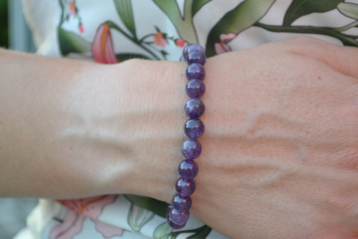 Bracelet Améthyste en pierre naturelle porté sur un poignet d'une femme au niveau du ventre. perle de diamètre 7-8mm