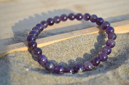 Bracelet Améthyste en pierre naturelle posé sur du sable à cheval sur un plateau en bois. perle de diamètre 5-6mm
