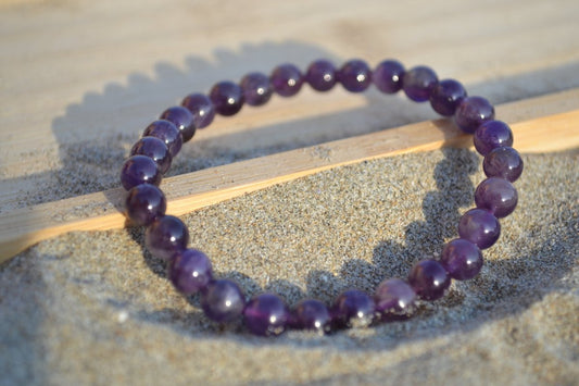 Bracelet Améthyste en pierre naturelle posé sur du sable à cheval sur un plateau en bois. perle de diamètre 5-6mm