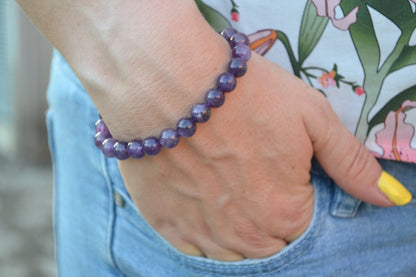 Bracelet Améthyste en pierre naturelle porté sur un poignet d'une femme au niveau de la hanche. perle de diamètre 7-8mm