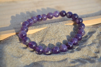 Bracelet Améthyste en pierre naturelle posé sur du sable à cheval sur un plateau en bois. perle de diamètre 7-8mm