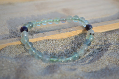 Bracelet Fluorite en pierre naturelle posé sur du sable à cheval sur un plateau en bois. perle de diamètre 5-6mm