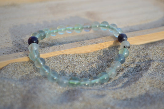 Bracelet Fluorite en pierre naturelle posé sur du sable à cheval sur un plateau en bois. perle de diamètre 5-6mm