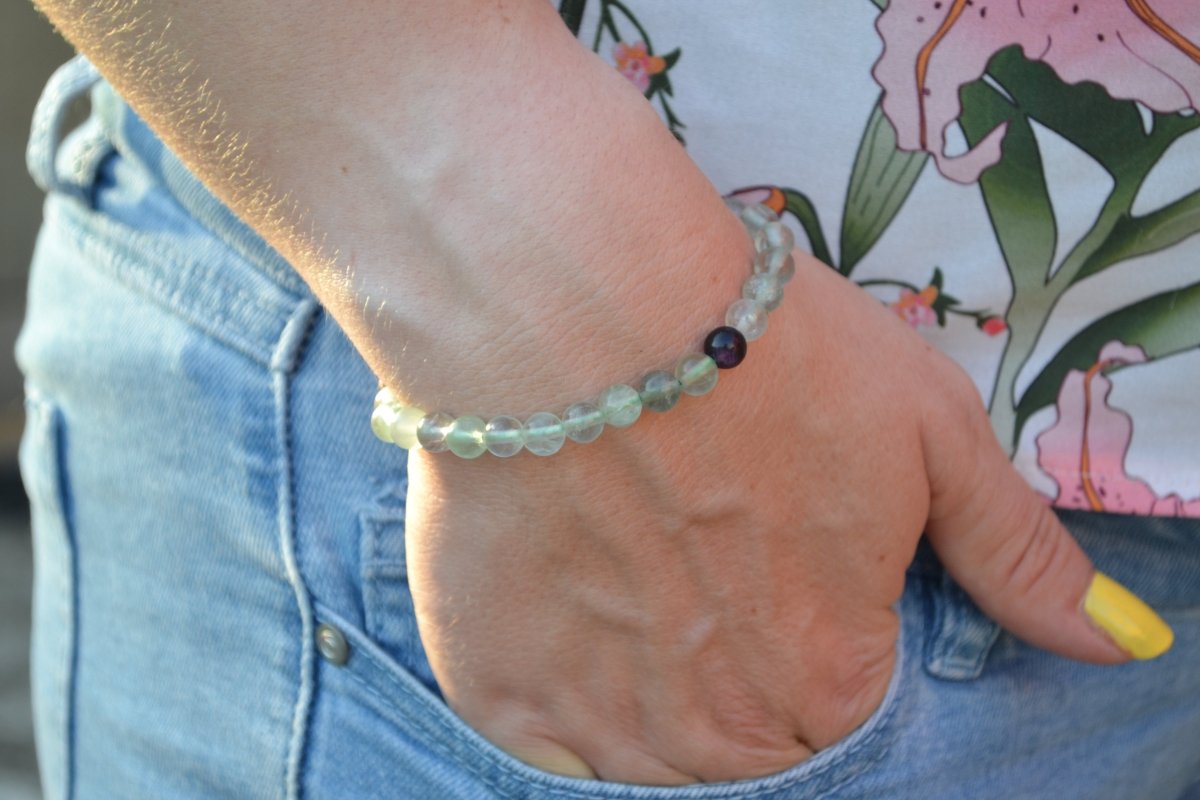 Bracelet Fluorite en pierre naturelle porté sur un poignet d'une femme au niveau de la hanche. perle de diamètre 5-6mm