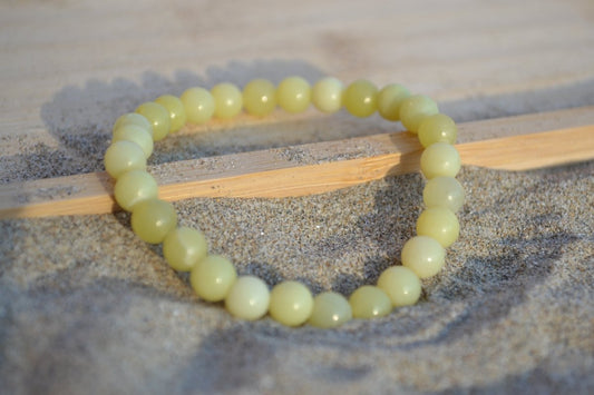 Bracelet Jade Citron en pierre naturelle posé sur du sable à cheval sur un plateau en bois. perle de diamètre 5-6mm