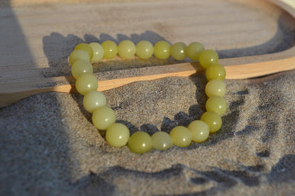 Bracelet Jade Citron en pierre naturelle posé sur du sable à cheval sur un plateau en bois. perle de diamètre 7-8mm