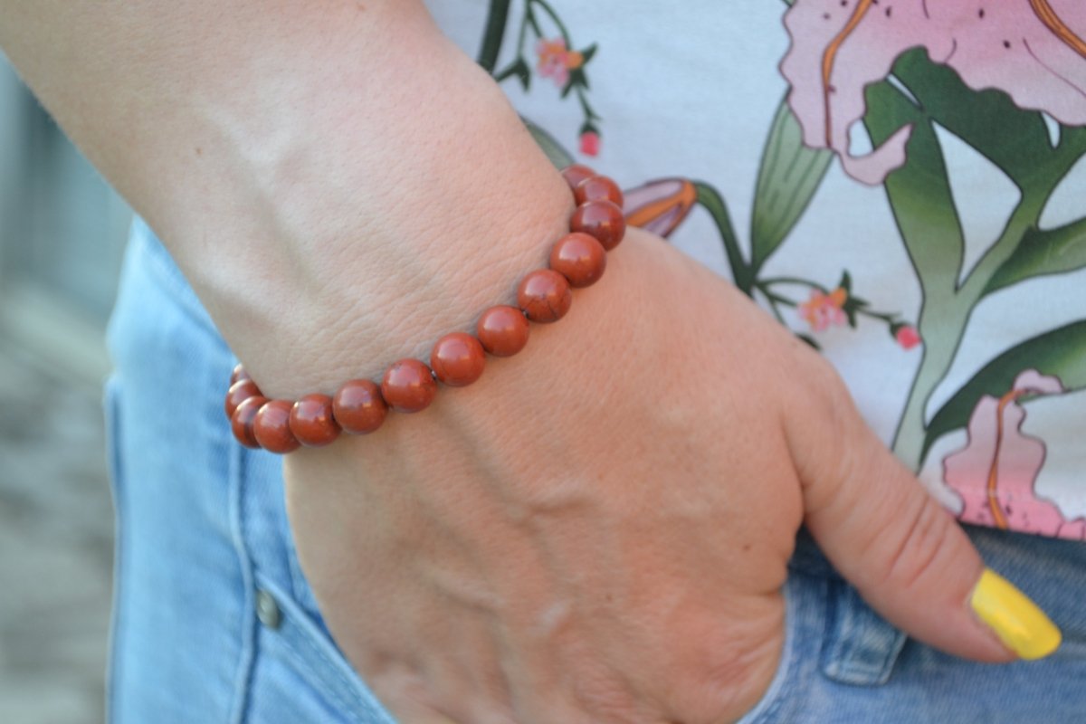 Bracelet Jaspe Rouge en pierre naturelle porté sur un poignet d'une femme au niveau de la hanche. perle de diamètre 7-8mm