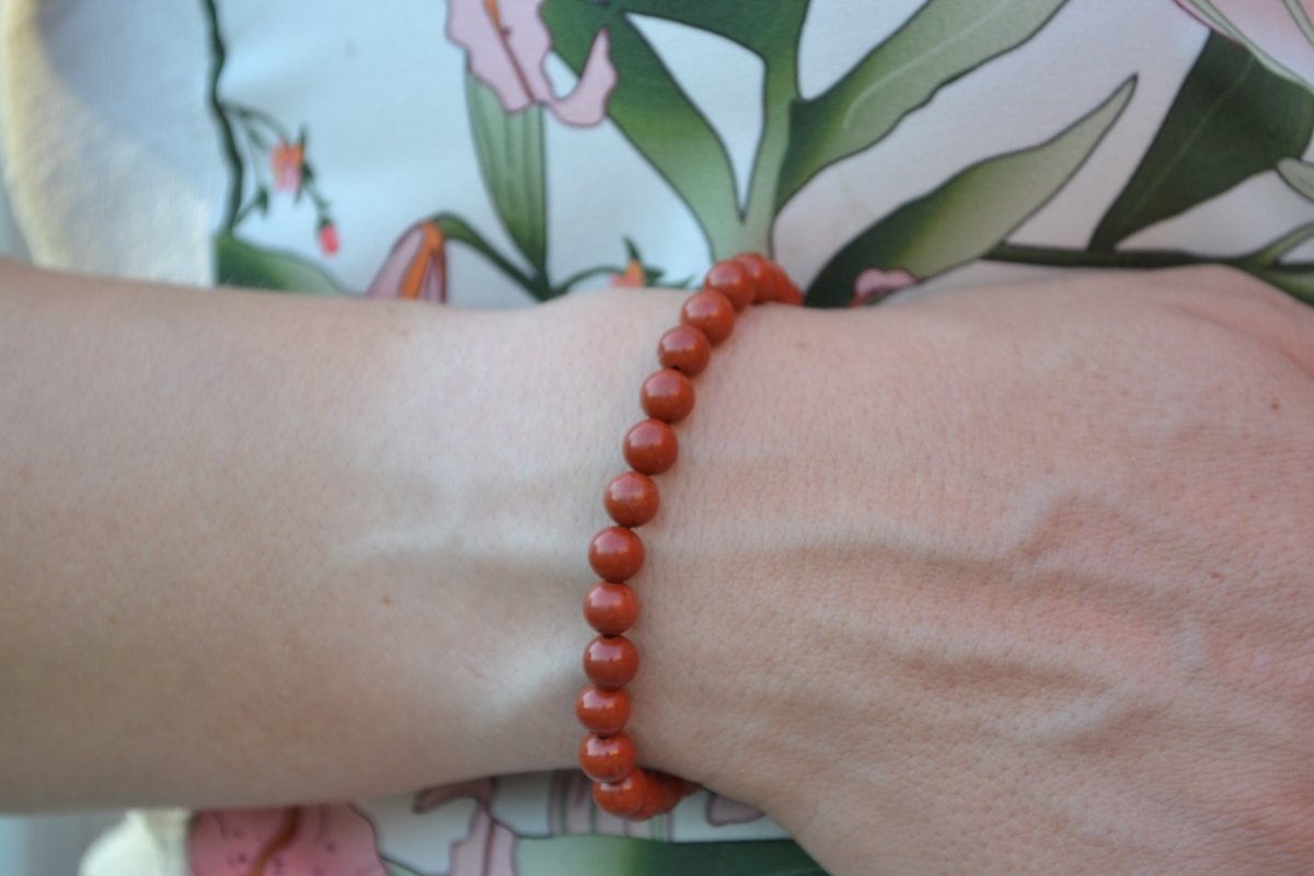 Bracelet Jaspe Rouge en pierre naturelle porté sur un poignet d'une femme au niveau du ventre. perle de diamètre 5-6mm