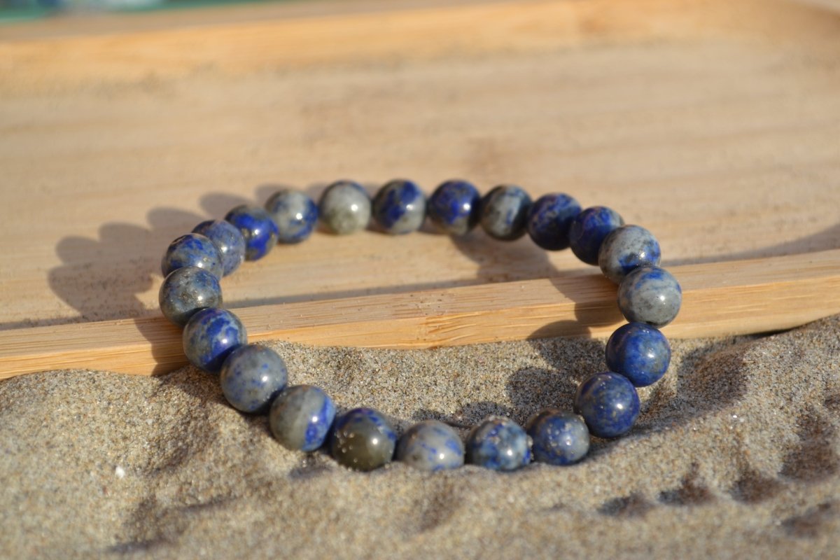 Bracelet Lapis Lazuli en pierre naturelle posé sur du sable à cheval sur un plateau en bois. perle de diamètre 7-8mm