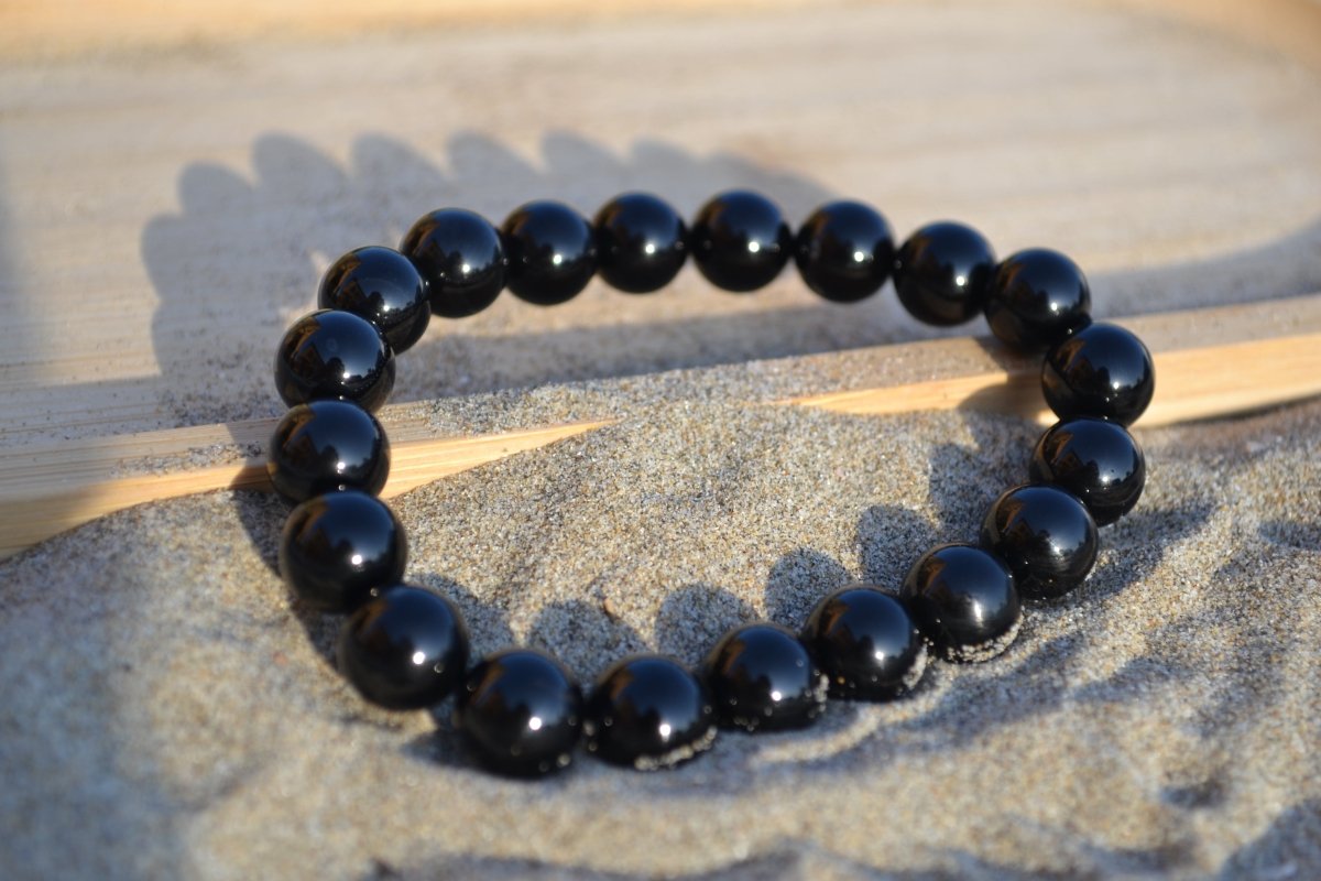 Bracelet Onyx en pierre naturelle posé sur du sable à cheval sur un plateau en bois. perle de diamètre 7-8mm