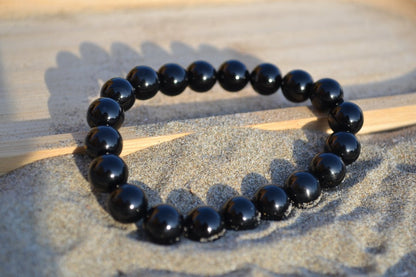 Bracelet Onyx en pierre naturelle posé sur du sable à cheval sur un plateau en bois. perle de diamètre 7-8mm