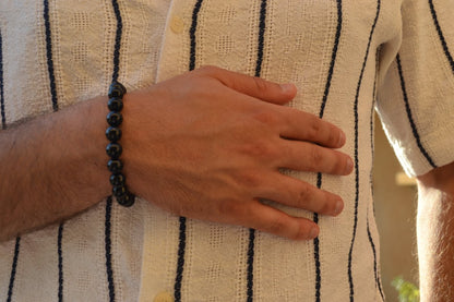 Bracelet Onyx en pierre naturelle porté sur un poignet d'un homme au niveau du ventre. perle de diamètre 7-8mm