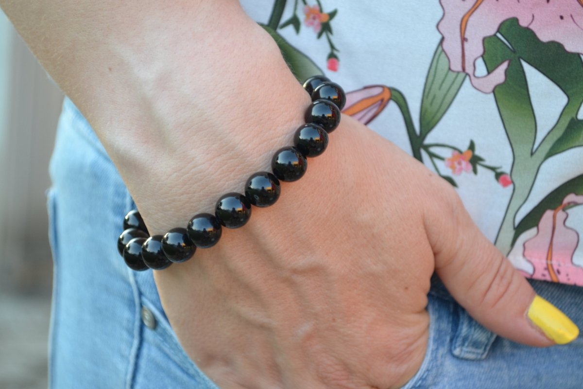Bracelet Onyx en pierre naturelle porté sur un poignet d'une femme au niveau de la hanche. perle de diamètre 7-8mm