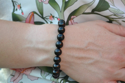 Bracelet Onyx en pierre naturelle porté sur un poignet d'une femme au niveau du ventre. perle de diamètre 7-8mm