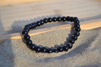 Bracelet Onyx en pierre naturelle posé sur du sable à cheval sur un plateau en bois. perle de diamètre 5-6mm