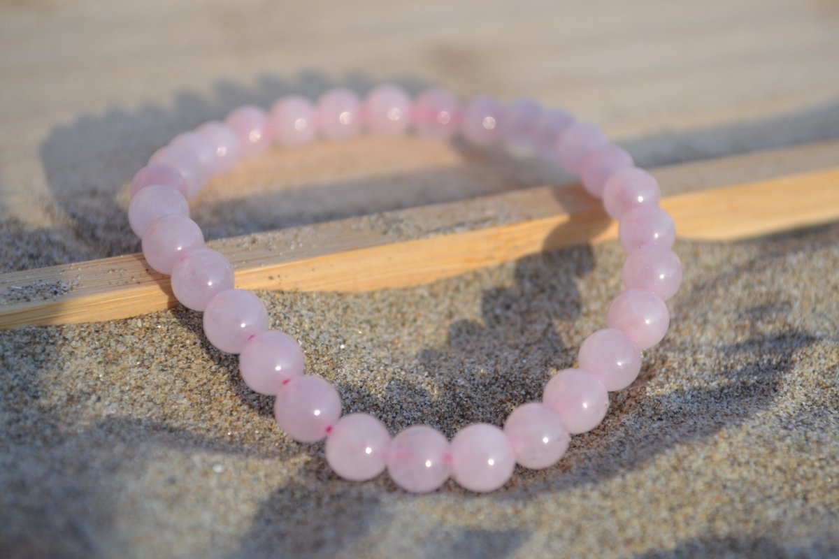 Bracelet Quartz Rose en pierre naturelle posé sur du sable à cheval sur un plateau en bois. perle de diamètre 5-6mm