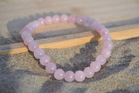 Bracelet Quartz Rose en pierre naturelle posé sur du sable à cheval sur un plateau en bois. perle de diamètre 5-6mm