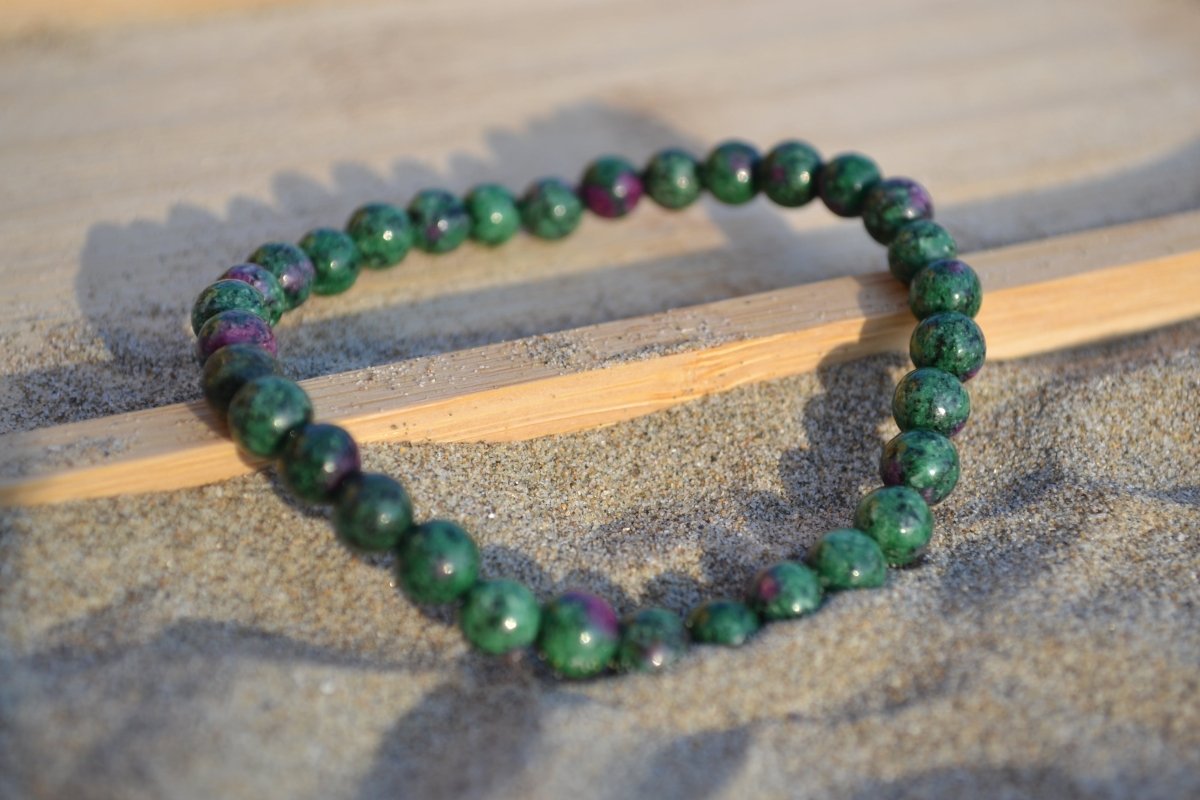 Bracelet Rubis Zoïsite en pierre naturelle posé sur du sable à cheval sur un plateau en bois. perle de diamètre 5-6mm