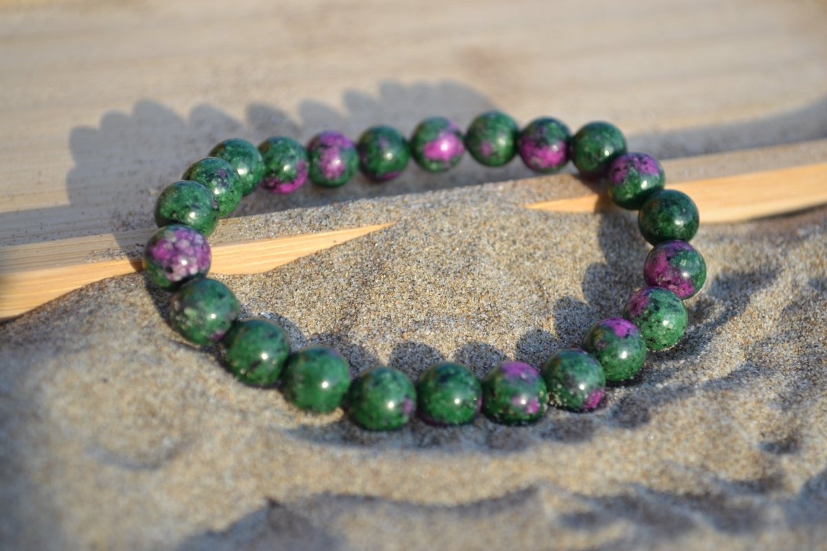 Bracelet Rubis Zoïsite en pierre naturelle posé sur du sable à cheval sur un plateau en bois. perle de diamètre 7-8mm