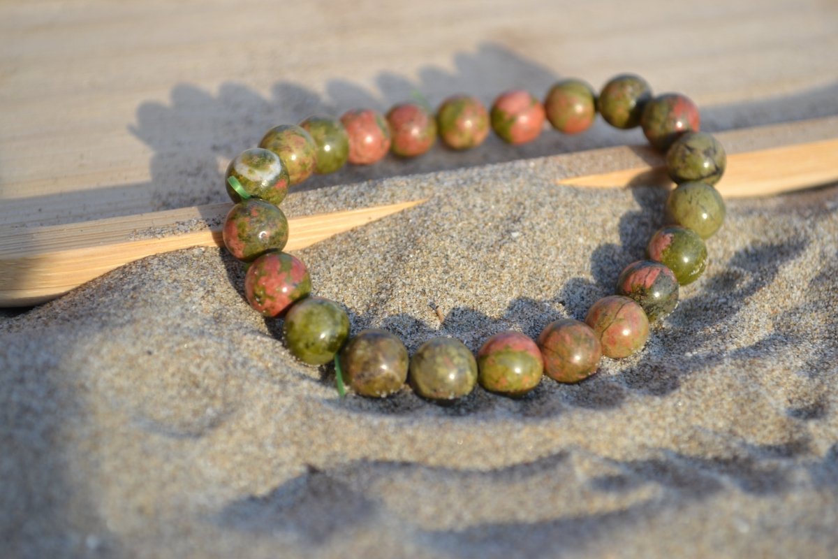 Bracelet Unakite en pierre naturelle posé sur du sable à cheval sur un plateau en bois. perle de diamètre 7-8mm
