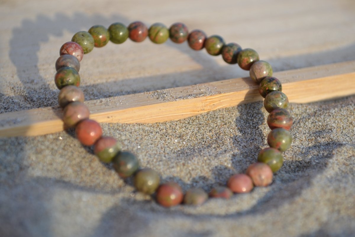 Bracelet Unakite en pierre naturelle posé sur du sable à cheval sur un plateau en bois. perle de diamètre 5-6mm